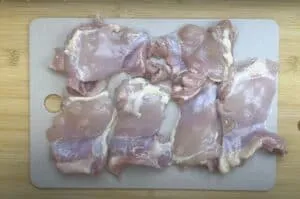 Raw chicken thighs on a cutting board, ready for cooking preparation.